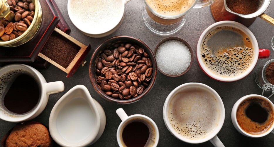 Mesa con granos de café, leche, azúcar y bebidas que se pueden preparar con café.